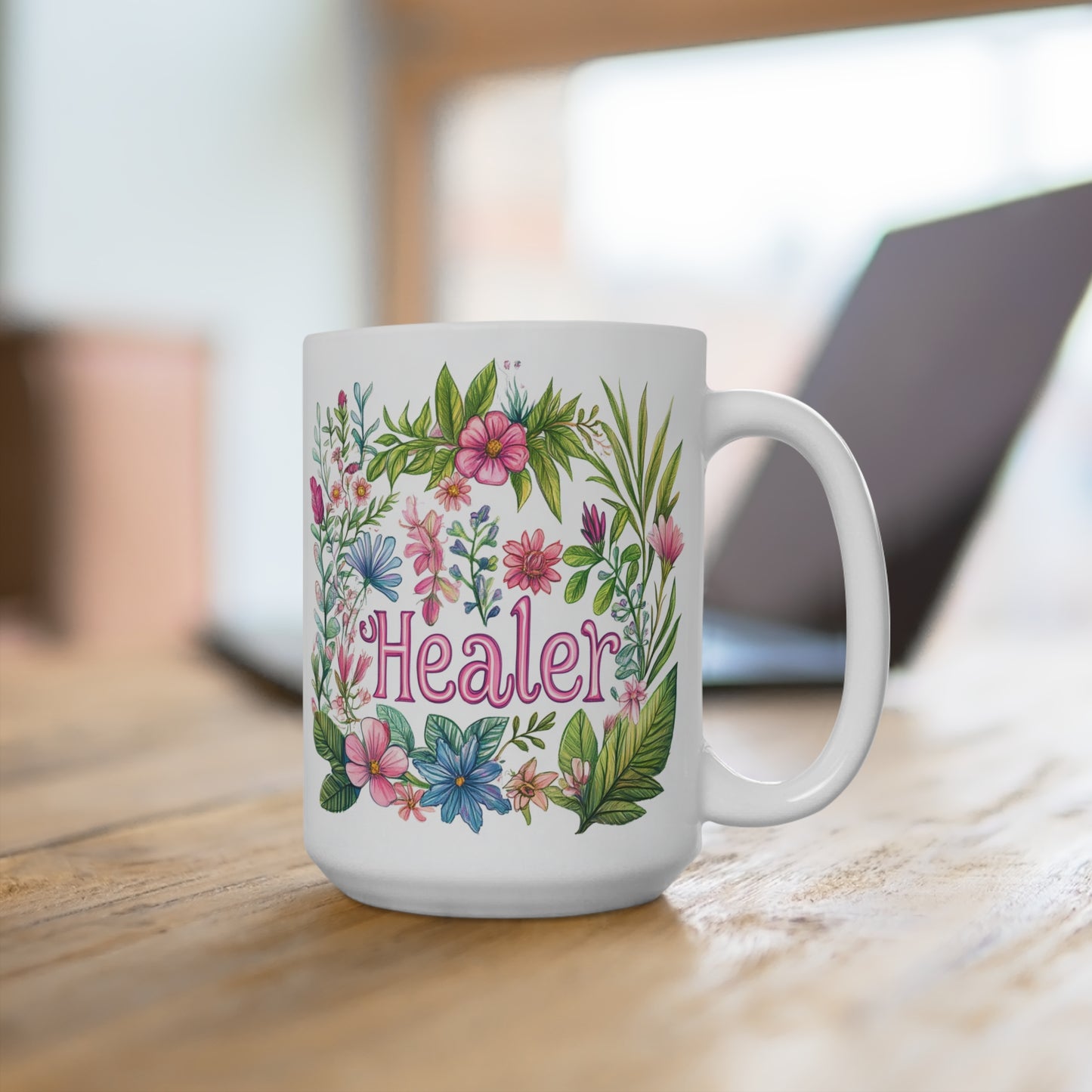 White ceramic healer mug with pink script and colorful floral wreath design on wooden desk