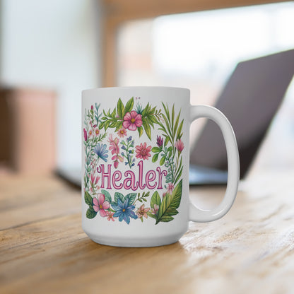 White ceramic healer mug with pink script and colorful floral wreath design on wooden desk