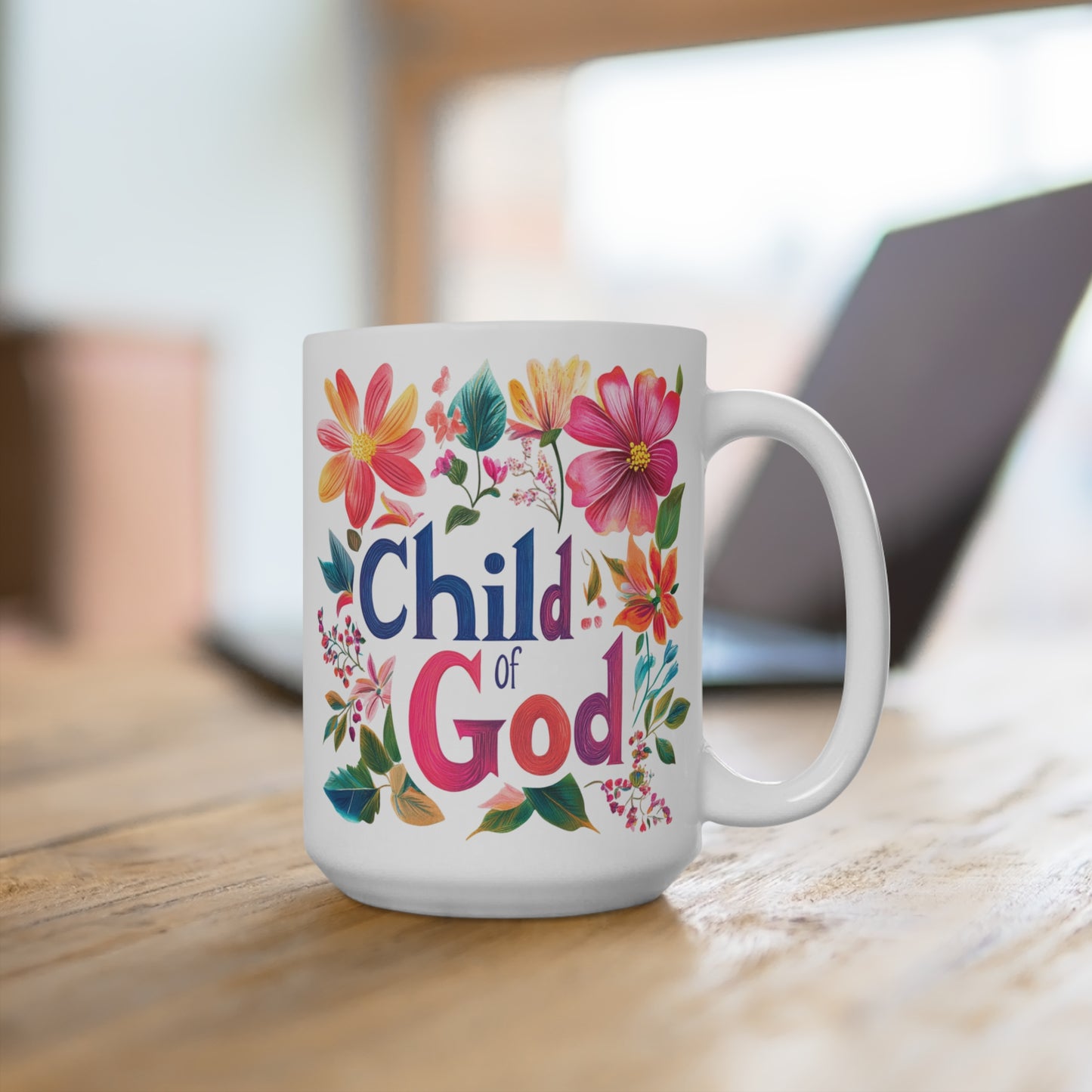 White ceramic child of God mug with colorful flowers on wooden table in home office setting